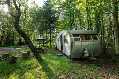 an old airstream trailer parked in the woods at The Outlier Inn in Woodridge