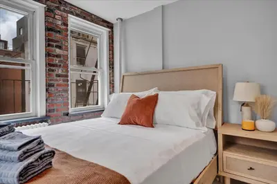 a bedroom with a white bed with a brick wall at SoHo Designer 2BR w balcony in New York