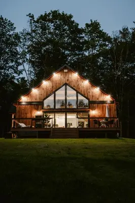 a large wooden house with lights on it at Luxe Modern Cabin with Pond, Fire Pit, Hiking, near Bethel Woods in Narrowsburg