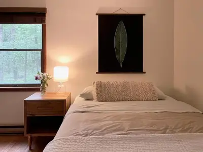 a bedroom with a bed and a lamp and a window at Fire Pit Woodsy & Private - Cabin on Woods Road in Yulan
