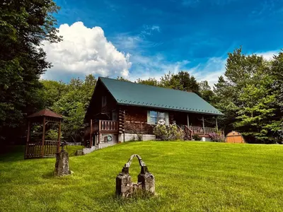 a log cabin on a grassy field in front of a house at Fire Pit, BBQ & Sprawling Lawn Elk Point Cabin in Livingston Manor
