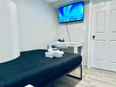 a room with a bed with a desk and a tv at Bright, Stylish and Comfortable Room with Workspace! in Haledon
