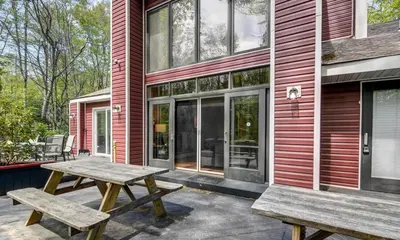 a patio with two picnic tables in front of a house at Hot tub, Sauna, fire pit, games and nature in Lake Poconos in Pocono Summit
