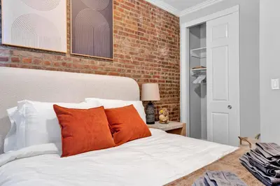 a bed with orange pillows and a brick wall at Modern 2BR with Private Garden - In Gramercy Park in New York