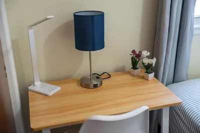 a desk with a lamp and flowers on it at Spacious Apartment - 3 min Train to NYC in Bayonne
