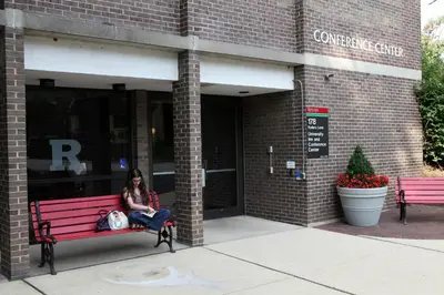 a woman sitting on a red bench in front of a building at Rutgers University Inn and Conference Center in New Brunswick