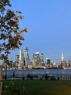 a city skyline with people sitting on benches in a park at Luxury duplex - 10 min to NYC/Times Square in Hoboken