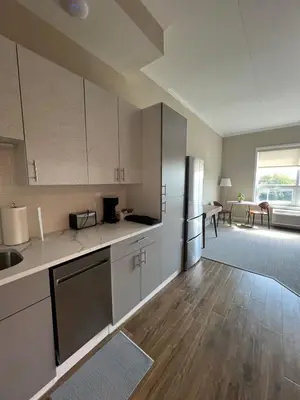an empty kitchen with white cabinets and a living room at 410 Modern Brand New Studio Apartment in Old Bridge