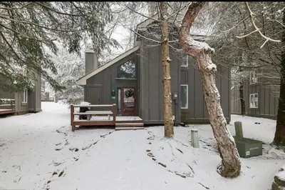 a house with a bench in the snow at Amazing Condo with hot tub and screened in porch 8 passes to lake and beach in Stoddartsville