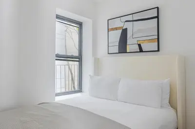 a white bedroom with a bed and two windows at Blueground Alphabet City view nr Tompkins Sq Park NYC-1884 in New York