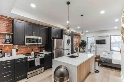 a kitchen with black cabinets and a brick wall at Large Studio w 2 Beds and Balcony (C) in Philadelphia