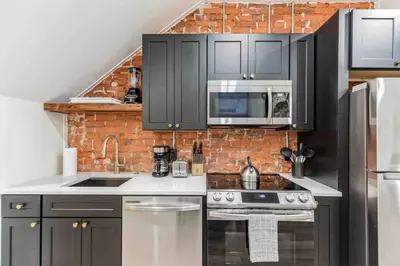 a kitchen with black cabinets and a brick wall at Large Studio w 2 Beds and Balcony (C) in Philadelphia