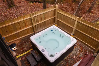 a hot tub in a backyard with a fence at Winter retreat, hot tub, game room, indoor pool, in Long Pond