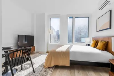 a bedroom with a bed and a desk and windows at Blueground Alphabet City rooftop nr Tompkins Square Park NYC-2081 in New York
