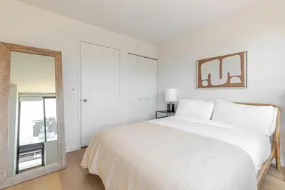 a white bedroom with a large bed and a mirror at Blueground Upper West Side fitness nr Central Park NYC-1994 in New York