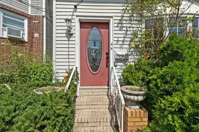 a red door on a white house with a porch at Quiet Retreat 10 Min to NYC Train & free Parking in Bayonne