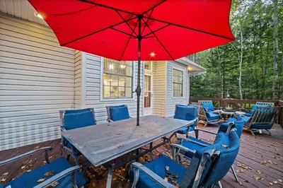 a table and chairs with a red umbrella on a deck at Pocono Lake Escape, includes Golf Cart, Firepit in Pocono Lake