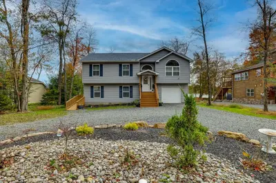 a house with a gravel driveway in front of it at Lakefront Pocono Retreat with Hot Tub and Movie Hub in Pocono Summit