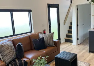 a living room with a brown couch and some windows at Scenic Ridge Haven Firepit, Trails & Views