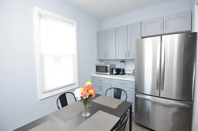 a kitchen with a table and a stainless steel refrigerator at Cozy Beds with Parking, Laundry - Near RU, RWJ, NJ Transit in Highland Park