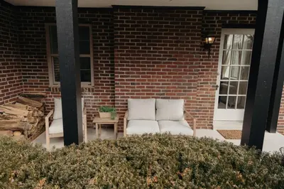 a porch with two white chairs and a brick building at Lady Grey Cottage - Hot Tub in Conestoga