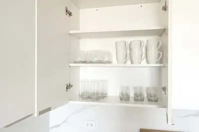 a white cupboard with glasses and cups on it at Luxe Loft 15 Min from NYC with City View & Gym in Jersey City