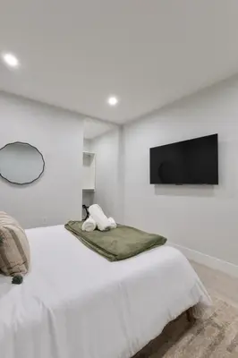 a white bedroom with a bed and a flat screen tv at Luxe Loft 15 Min from NYC with City View & Gym in Jersey City