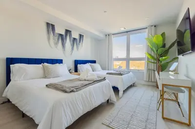 a white bedroom with two beds and a desk at Sleek Loft 15 Min from NYC with Manhattan View in Jersey City
