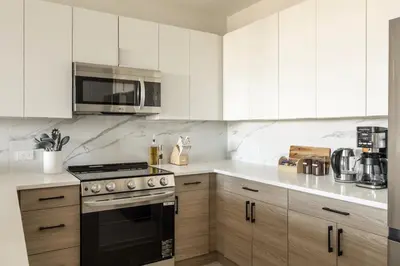 a kitchen with white cabinets and a stove and microwave at Sleek Loft 15 Min from NYC with Manhattan View in Jersey City