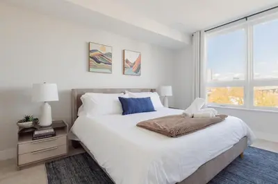 a white bedroom with a large bed and a window at Sleek Loft 15 Min from NYC with Manhattan View in Jersey City