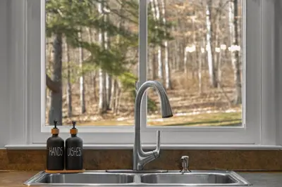two bottles of wine sitting on a kitchen sink in front of a window at Peaceful Valley Retreat in Elliottsburg