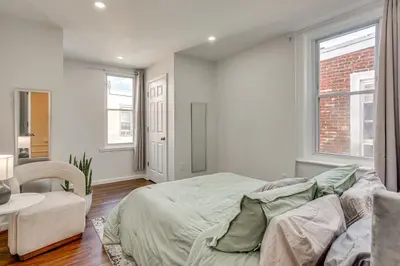 a bedroom with a bed and a chair and windows at 3-Story Rowhouse with Patio! 5 Mi to Center City in Philadelphia