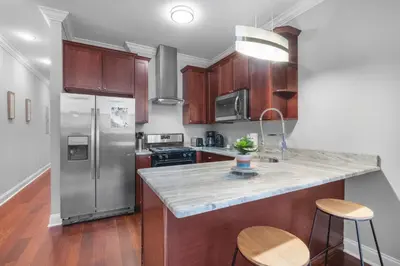a kitchen with wooden cabinets and a stainless steel refrigerator at Luxury Studio Loft - Rooftop View & Pool in Philadelphia