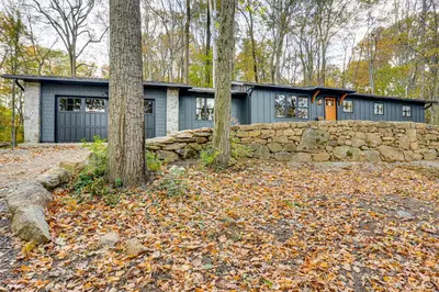 a house with a stone retaining wall and trees at Serene Getaway with Trail Access in Chester Springs in Chester Springs