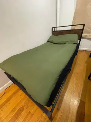 a bed with a green comforter on a wooden floor at Union Square Studio with Kitchen -Shared Bathroom in New York