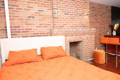a bed with orange pillows in front of a brick wall at West Village Escape - Steps from Subway Cafes in New York