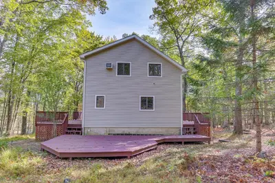 a white house with a deck in the woods at 6 Mi to Bushkill Falls Secluded Home with Game Room in East Stroudsburg