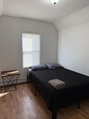 a bedroom with a black bed and a window at Private house with 4 bedrooms 2 bathrooms, NYC direct bus 1 block away, MetLife Stadium FIFA World Cup 30 minutes away in Perth Amboy