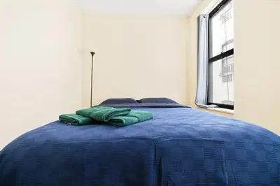 a bed with a blue comforter and a window at Spacious Central Park Apartments in New York