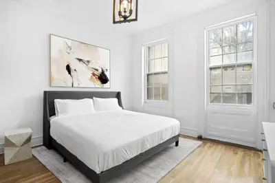 a white bedroom with a bed and two windows at Classic NYC Brownstone 2Br Apartment in Prime Chelsea in New York