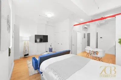 a white bedroom with a blue bed and a tv at Beautifully Renovated Studio in Prime Manhattan in New York