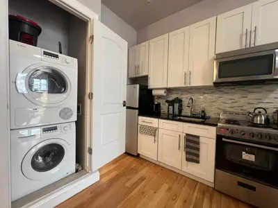 a kitchen with white cabinets and a washer and dryer at Cortland Manhattan Suites in New York