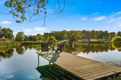 a person sitting on a bench on a dock on a lake at Pond Haven Retreat Wood-Burning HotTub & FirePit in Mount Bethel