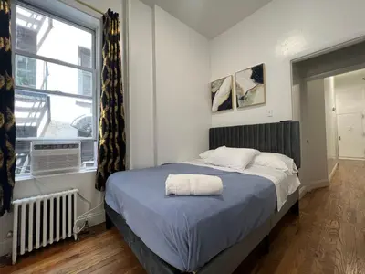 a bedroom with a bed with a blue blanket and a window at Parkline Suites Upper West Side in New York