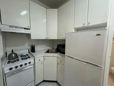 a kitchen with white cabinets and a white refrigerator at Parkline Suites Upper West Side in New York