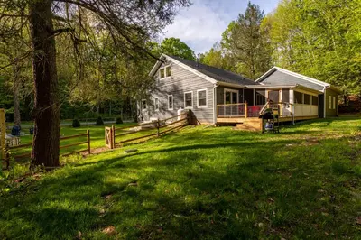 a house with a fence in front of a yard at Hare & Hollow with Hot Tub & Fenced Yard