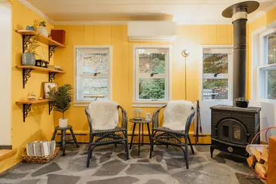 a yellow room with chairs and a table and a stove at Creekfront Cabin Sauna & Hot Tub Hikers Hollow in Cuddebackville