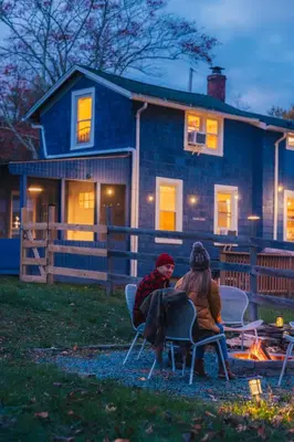 a woman and child sitting around a fire in front of a house at 1930's Vintage Cabin Hot Tub Kohler Cabin in Jeffersonville