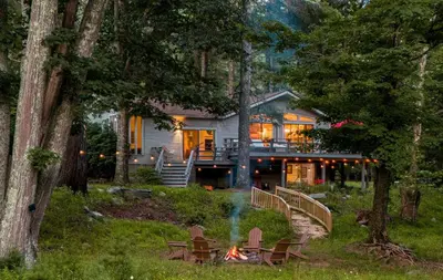 a house in the woods with a fire in the yard at Riverfront Retreat Hot Tub, Firepit & Pool Table in Cuddebackville