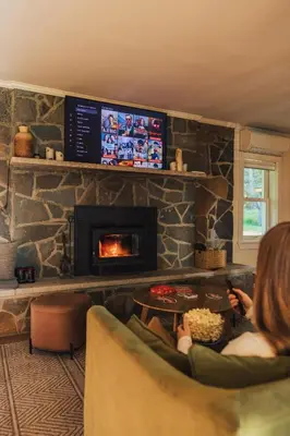 a woman sitting in a chair in a living room with a fireplace at Rivers Ledge Cabin with Sauna and Hot Tub in Barryville